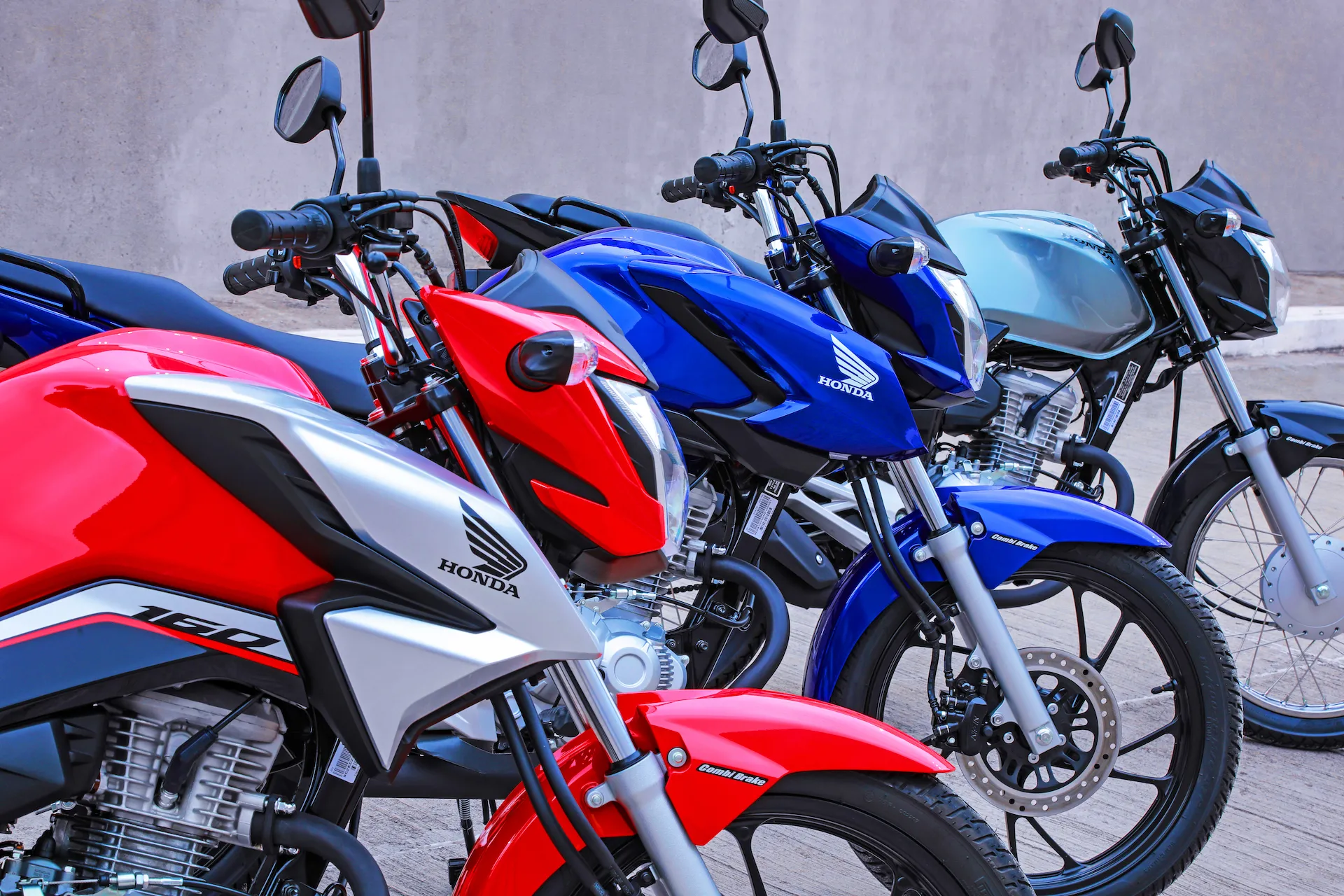 Três Honda CG 160 Fan enfileiradas nas cores vermelha, azul e prata