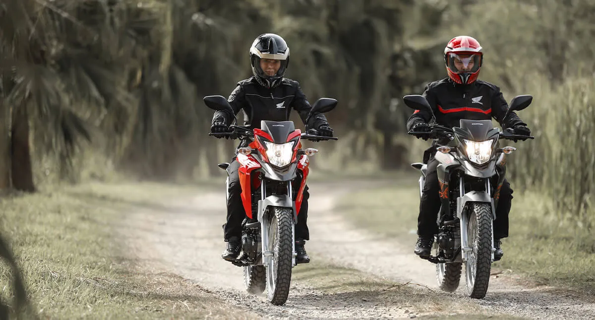 Dois pilotos em suas Motos Honda XRE 190 2024, uma vermelha e outra preta, em uma estrada de terra