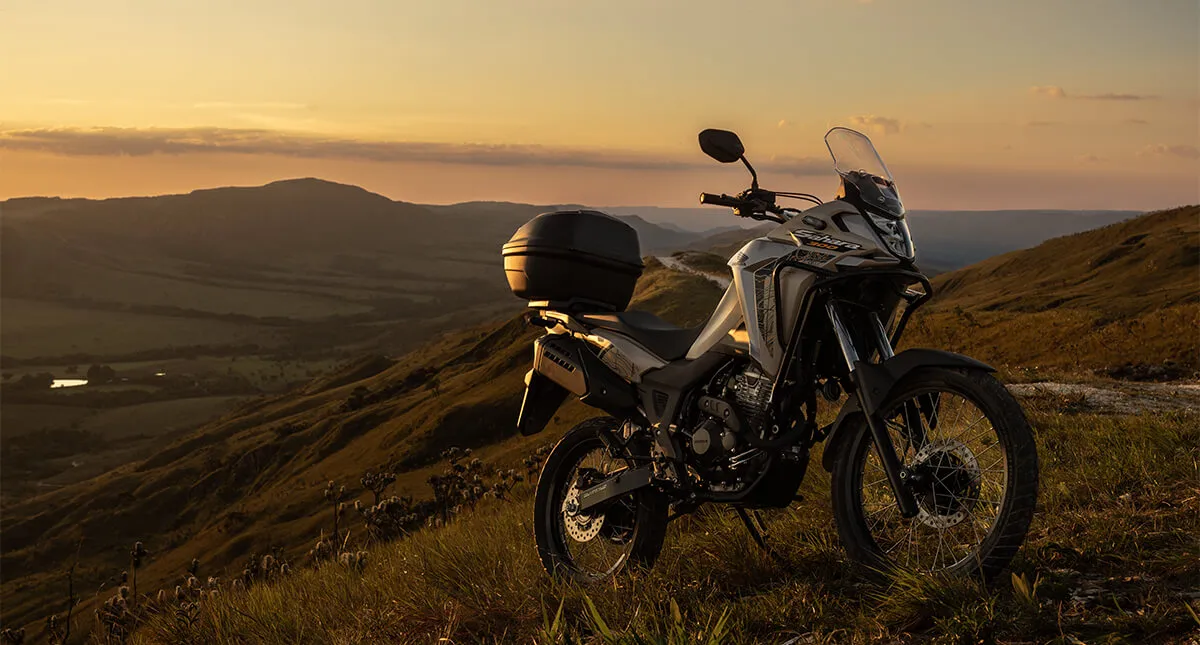 Nova Honda Sahara 300 prateada estacionada com deserto e pôr do sol ao fundo