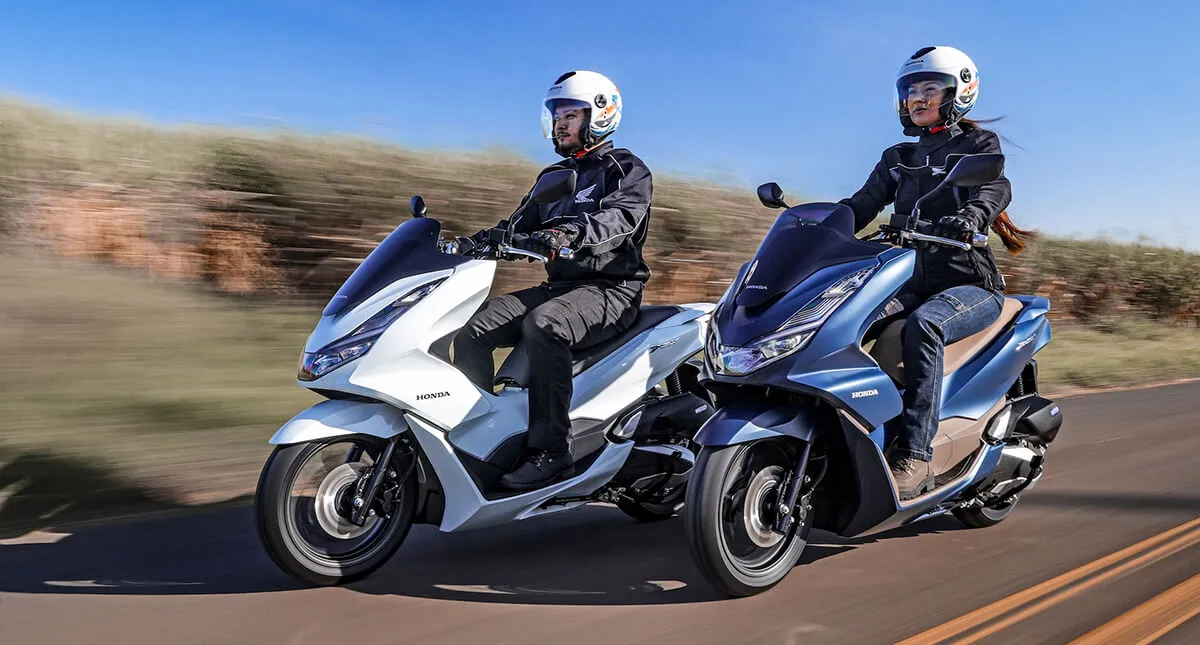Homem em scooter PCX  branca na estrada ao lado de mulher em scooter PCX azul