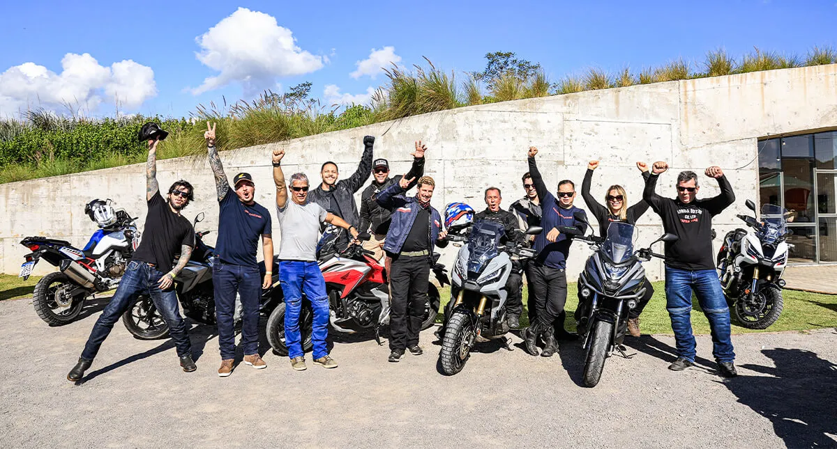 Grupo de pilotos com mãos para cima em vibração junto a suas motocicletas
