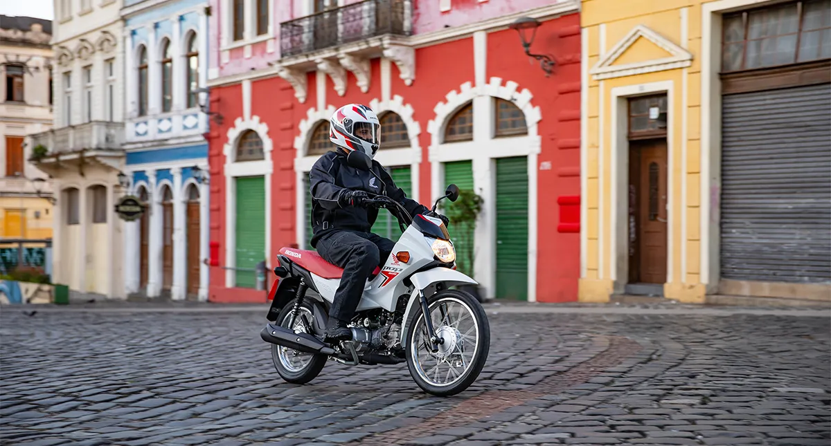 Motociclista pilotando a sua Honda POP 110i ES na rua de paralelepípedo