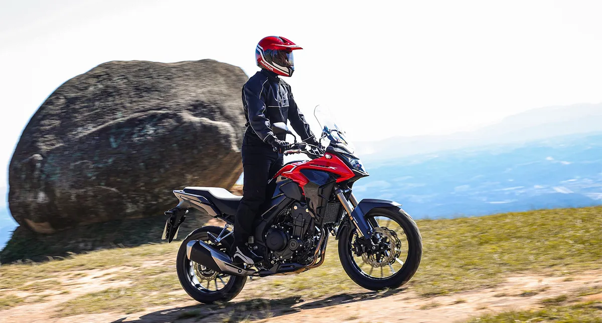 Piloto em sua Motocicleta Honda CB 500X vermelha em uma paisagem com uma grande pedra ao fundo