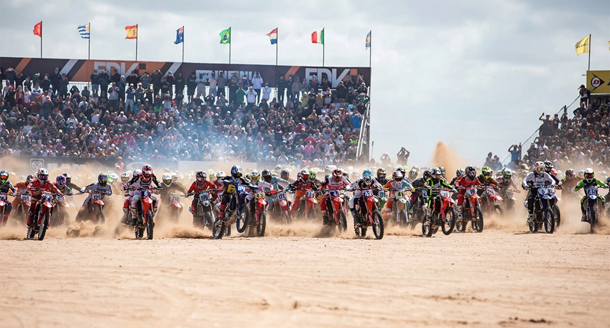 Pilotos iniciando a corrida no Enduro del Verano com uma grande multidão assistindo ao fundo