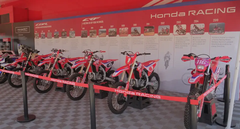 Exposição das motos off-road da equipe Honda Racing, com modelos alinhados e painel com imagens de piloto