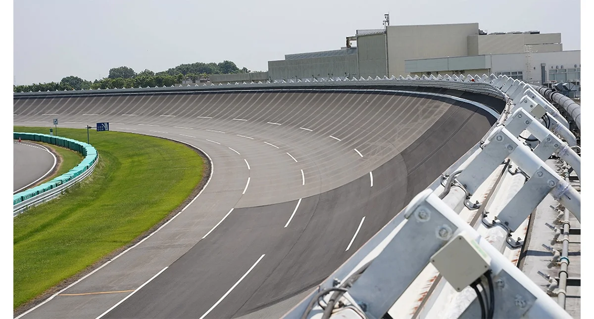 Pista oval inclinada em centro de testes, com prédios ao fundo